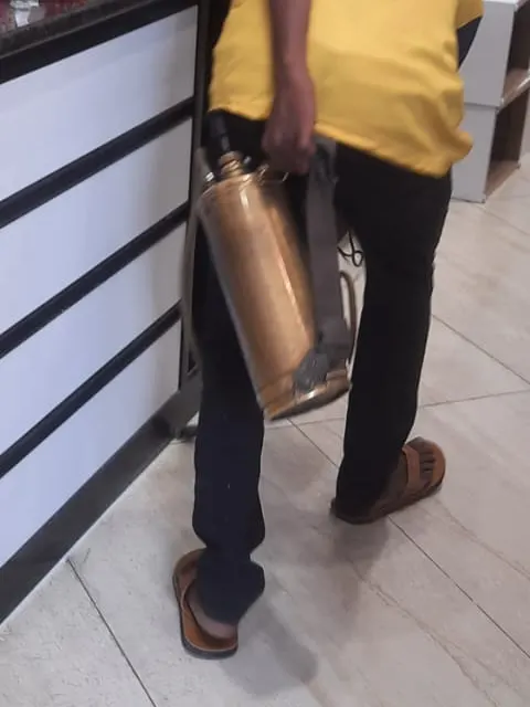 Technician carrying a pressure sprayer past a shop's display counter