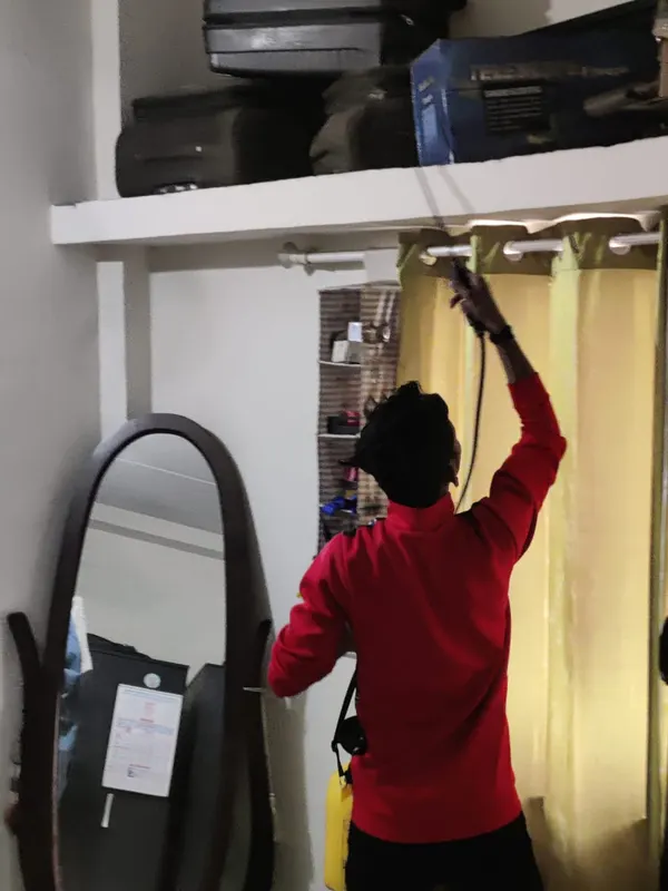 Technician reaching up to spray a bedroom curtain rail and loft shelf