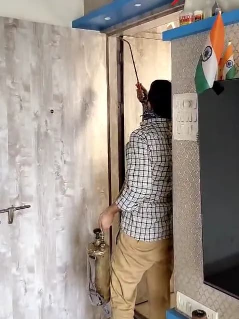 Pest control worker spraying the top edge of a flat's door frame